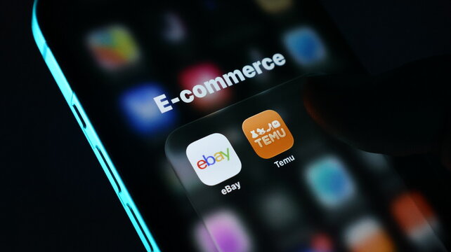Closeup of a smartphone screen showing ecommerce apps including ebay and temu icons, with a finger touching the screen