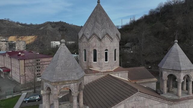 Aerial view of Saint Gregory of Narek Church in Kapan, showcasing its beautiful traditional tuff stone architecture, distinct domes, and scenic mountain landscape in the surrounding background