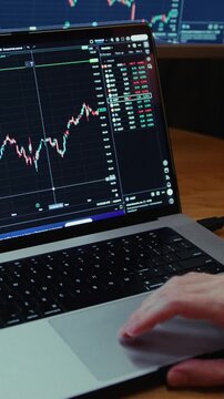 Man trader monitors market charts on laptop, screen and smartphone at home. Analyzing real-time trading data, considering investment strategies. Professional investor engaged in day trading, Evening