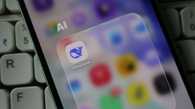Closeup of a smartphone screen displaying the deepseek ai application icon in a folder, with a blurred keyboard in the background