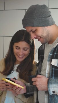 4K video of a young Hispanic couple drinking coffee while laughing and watching social media reels on their mobile phone. Concept of everyday lifestyle, emotional wellbeing, and a healthy romantic rel