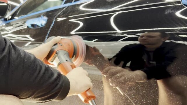 A car service worker polishes the car body with a polishing machine. Detailing and polishing of the car. Car detailing - hands with an orbital polishing machine in an auto repair shop. 
