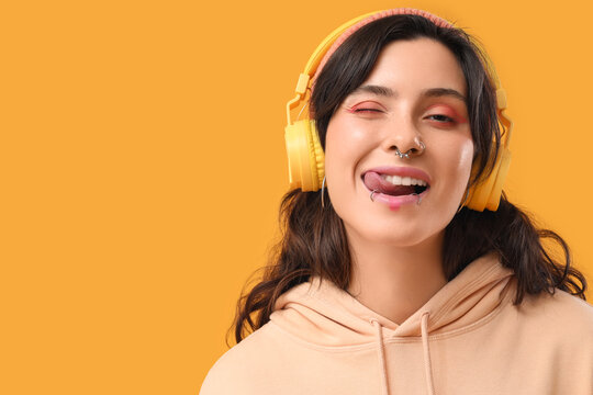 Happy young woman with face piercing listening to music on yellow background