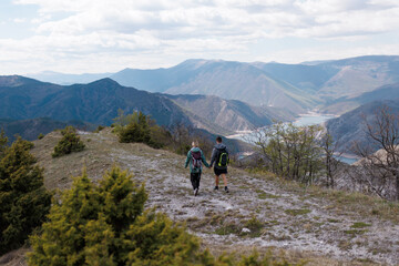 Fototapeta premium Friends hiking together along a mountain ridge overlooking a river valley with backpacks, enjoying an outdoor adventure and scenic panoramic views
