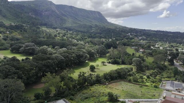 Drone flies backwards from golf course at base of mountain on a sunny day in Zomba, Malawi