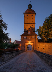Naklejka premium Historic Segringer Tor gate tower with cobblestone bridge illuminated at dusk. Dinkelsbuehl, Bavaria, Germany.