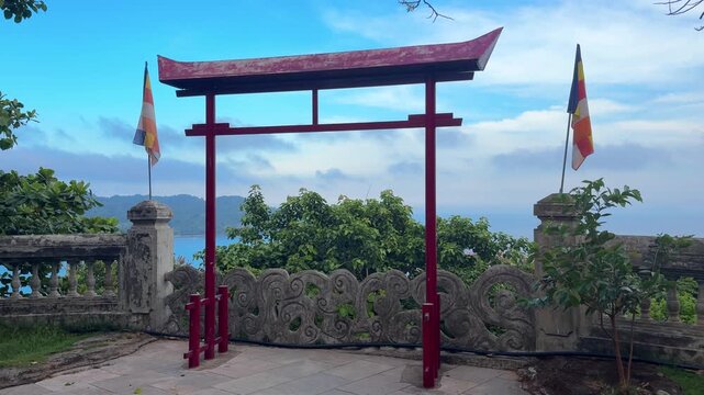 Video of a traditional red temple gate overlooking the sea in a tropical coastal setting. Scenic Asian cultural landmark representing Buddhism, spirituality, travel and architectural heritage.