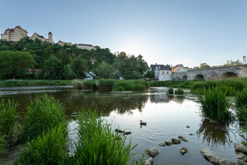 Fototapeta premium Historic castle on a hill overlooking a river with ducks, stone bridge and traditional houses. Harburg, Bavaria, Germany.