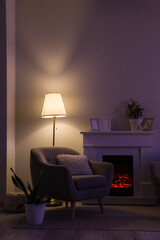 Fototapeta premium Interior of dark living room with glowing lamp, armchair and fireplace at night