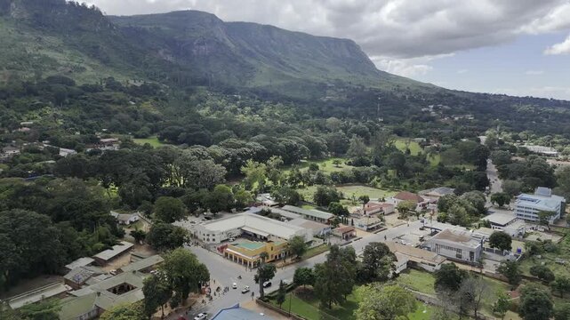 Drone flies left along main highway at base of mountain on a sunny day in Zomba, Malawi