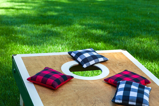 Low angle view of a corn hole board on grass with plaid bean bags on a sunny summer day