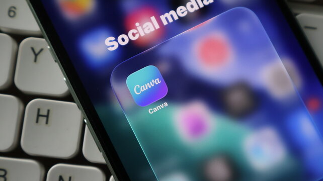 Closeup of a smartphone screen showing the canva app icon inside a social media folder, with a computer keyboard visible in the background