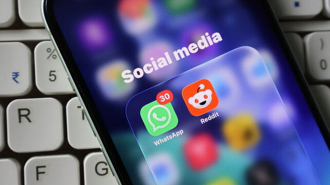 Closeup of a smartphone screen showing social media app icons including whatsapp and reddit with a notification badge on a keyboard background