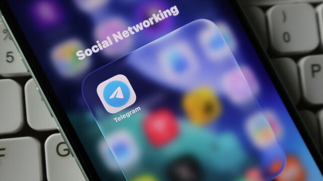 Closeup of a smartphone screen displaying the telegram app icon within a social networking folder, set against a blurred background