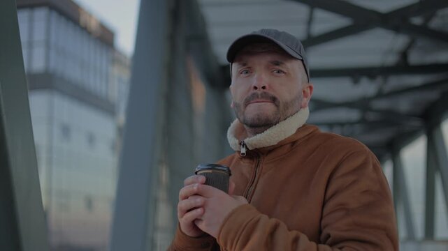 This high-resolution 4K video captures a detailed close-up of a man standing on a modern pedestrian bridge. The cinematic footage beautifully showcases the rich textures of his brown shearling jacket 