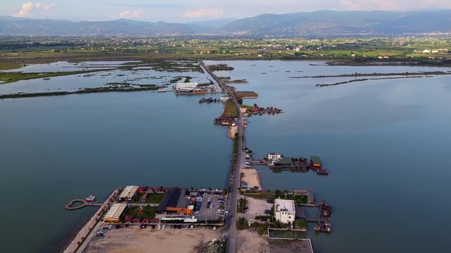 Aerial video featuring a unique wooden stilt cabins, seaside restaurants, and a road cutting through the calm waters of Patok Lagoon, Albania.