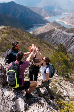 Group of friends hiking in the mountains celebrating with a high five on a rocky trail overlooking a turquoise lake and dramatic ridgelines