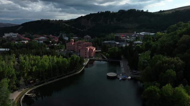 An aerial drone view of the scenic bridge stretching across a deep, green canyon in the resort town of Jermuk, Armenia, surrounded by beautiful mountains under dramatic clouds.

