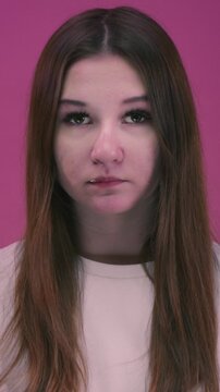 Vertical: Cute teen girl hold ripe yellow banana and eats. Portrait: teenager woman biting off banana on pink background. healthy eating fruits. Young female feeds good food, healthy snack for school