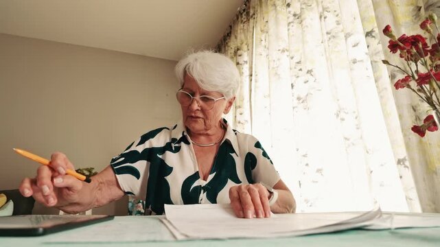Senior Woman Checking Household Bills and Documents at Table  