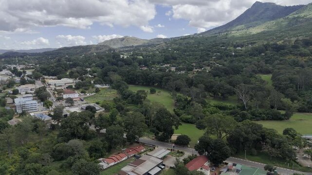 Drone facing south, flies to the right over main highway next to golf course at base of mountain on a sunny day in Zomba, Malawi