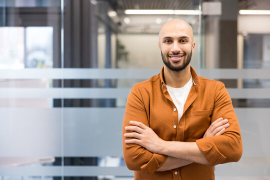 Confident bald man smiling with crossed arms in office