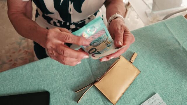 Senior Woman Counting Euro Banknotes and Coins at Table 