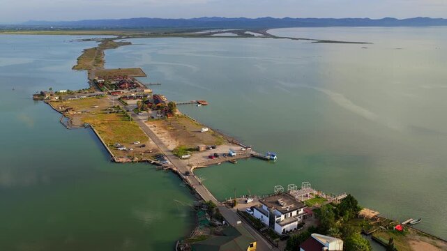 Aerial video featuring a unique wooden stilt cabins, seaside restaurants, and a road cutting through the calm waters of Patok Lagoon, Albania.