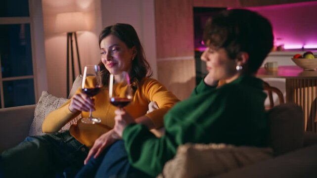 Bonding women drinking wine sitting cozy couch closeup. Smiling ladies clinking