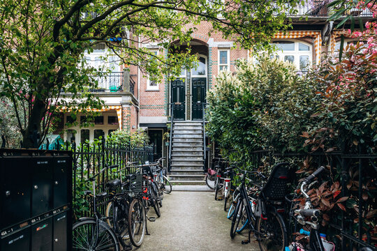 Amsterdam, Netherlands - April 18, 2026: Traditional Amsterdam East residential entrance with brick facade, bicycles, mailboxes and a green courtyard pathway 