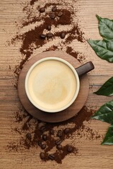 Naklejka premium Cup of aromatic coffee, leaves and ground beans on wooden table, flat lay