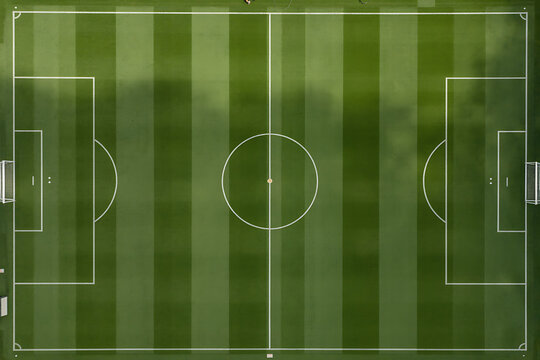 Aerial view of professional soccer field showing green grass pitch with white boundary lines and markings including center circle and penalty areas ready for competitive sports event.