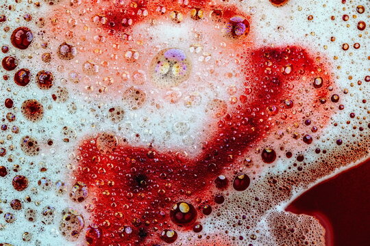 Schiuma da detergente con bolle e bollicine colorate in liquido rosso