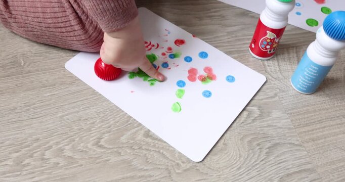 Close-up: toddler finger touches green sponge tip of marker and draws with it. Little child explores textures of colorful paints during creative activity at home. Concept for fine motor development