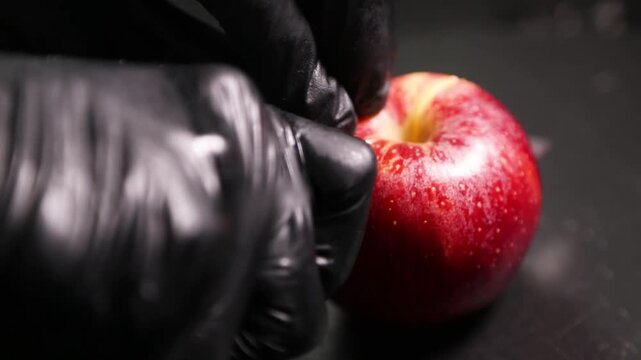 Chef profesional con guantes negros cortando una manzana roja fresca. Preparaci&oacute;n culinaria artesanal, ingrediente gourmet.