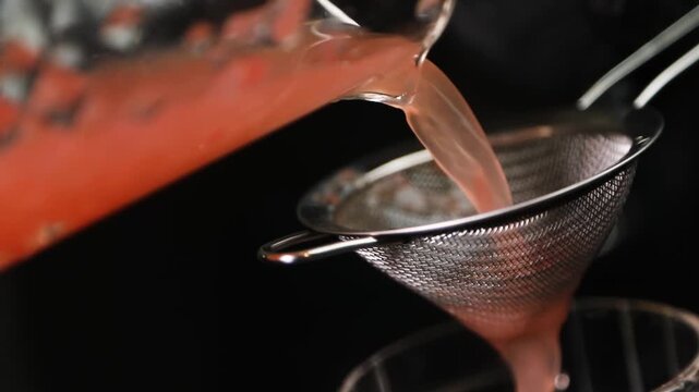 Barman colando l&iacute;quido con colador met&aacute;lico sobre fondo negro. Barman profesional filtrando un c&oacute;ctel con un colador met&aacute;lico. C&oacute;ctel artesanal, t&eacute;cnica de bar precisa, servicio de primera.