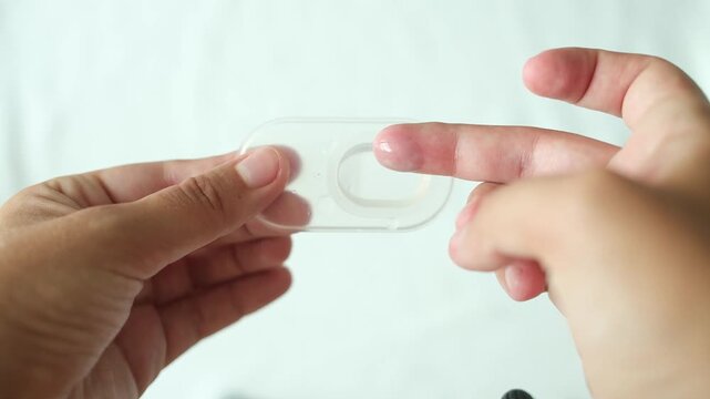 Hands opening and touching contact lens blister pack on white background in top view close up. Minimal healthcare and eye care concept with clean aesthetic composition and optical product packaging
