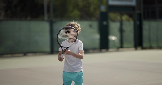 Focused young child swings a racket at a tennis ball on an outdoor court, showcasing concentration and youthful energy.