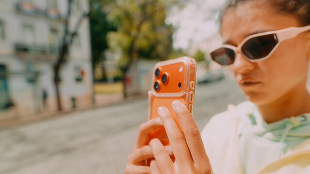 Young woman creator shooting street selfie with orange smartphone