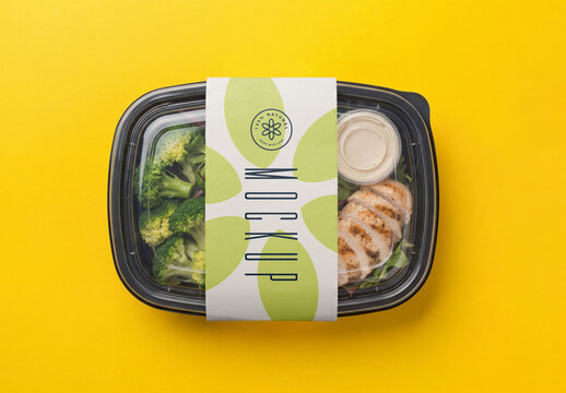 Top view of a plastic meal prep container mockup with chicken and broccoli salad wrapped in a paper sleeve label isolated on a yellow background