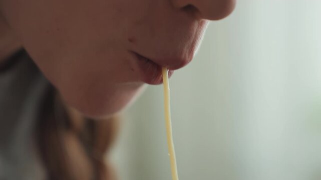 Intimate noodle tasting. Detailed image of lips delicately tasting single strand of noodle. Intimate scene showing softlit kitchen environment with quietly savoring diner and visible braid