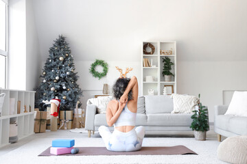 Sporty mature woman in reindeer horns doing yoga at home on Christmas eve, back view © Pixel-Shot