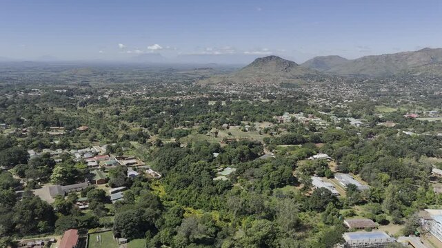 Drone flies east from base of mountain toward city on a sunny day in Zomba, Malawi