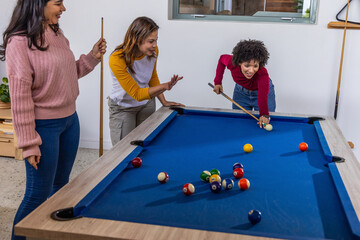 Fototapeta premium Diverse female friends lining up pool shot on blue-felt table in game room holding cues