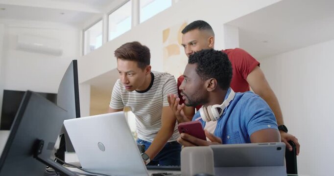 Diverse male team leaning and studying laptop as seated man showing pink smartphone, reviewing code