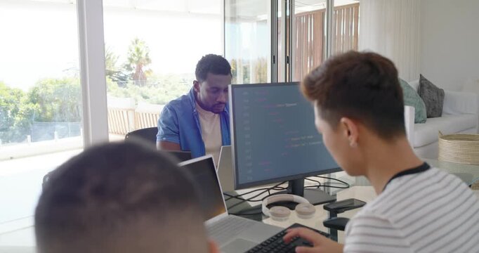 Diverse male coworkers celebrating in home office after code success on monitor, high-fiving