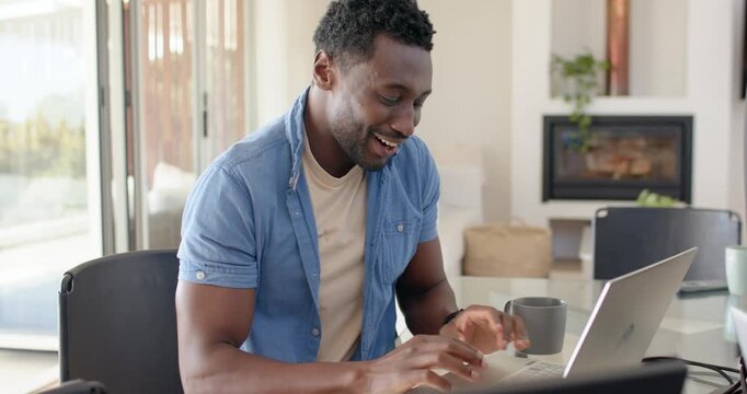 African mid-adult man wearing light blue shirt watching laptop content, leaning in, typing to reply