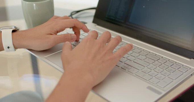Asian man starting task, typing steadily on silver laptop at home office desk with white wristband