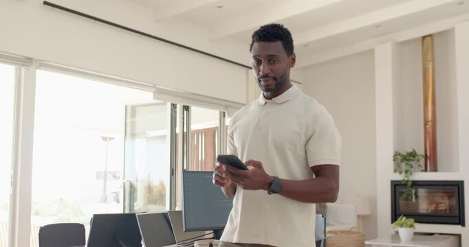 After phone alert African American mid-30s man walking into home office scrolling phone, smiling