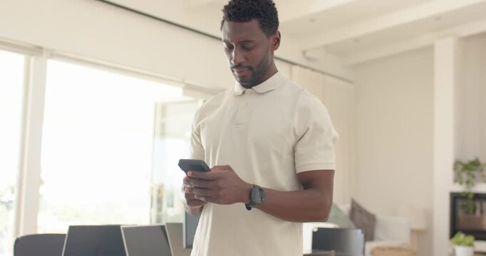 Mid adult African man checking smartphone, scrolling and smiling while reading text in home office